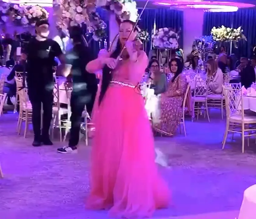 Violinist in a pink gown playing in a packed party room