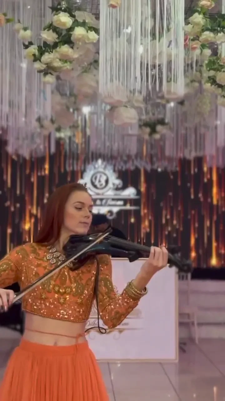 Violinist in an orange outfit playing a Bollywood love song