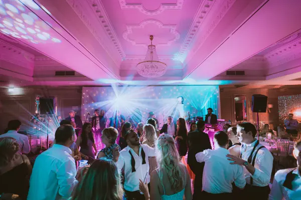 Packed dancefloor under pink lighting with a live band