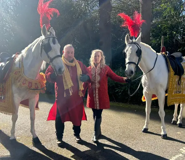 Two white wedding horses with handlers in traditional dress