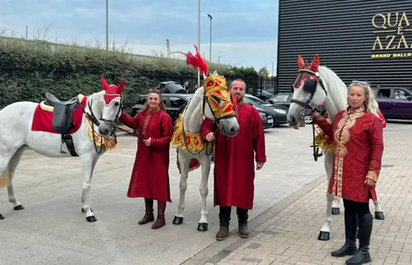 Three decorated white horses with handlers outside a banqueting hall