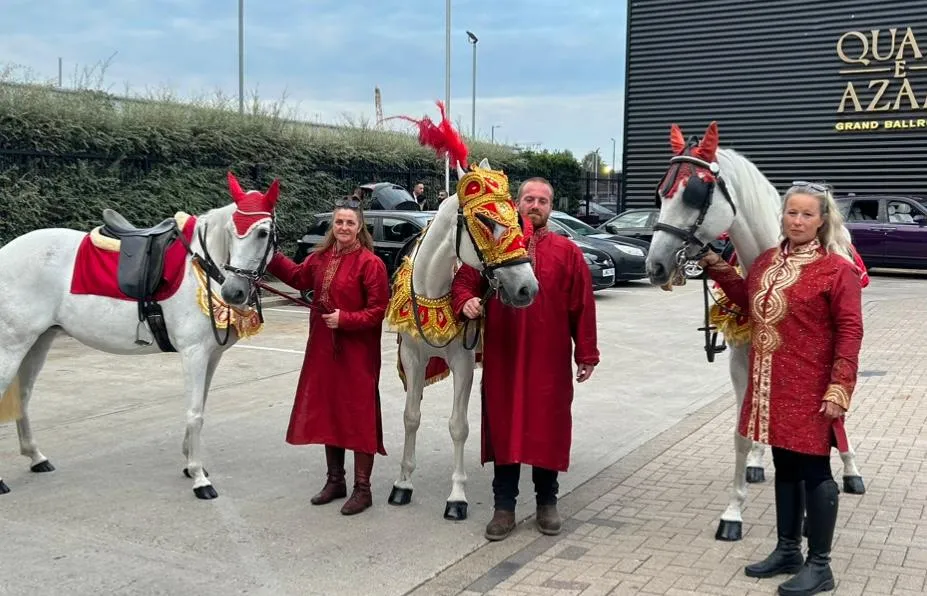 Three decorated white horses with handlers outside a banqueting hall