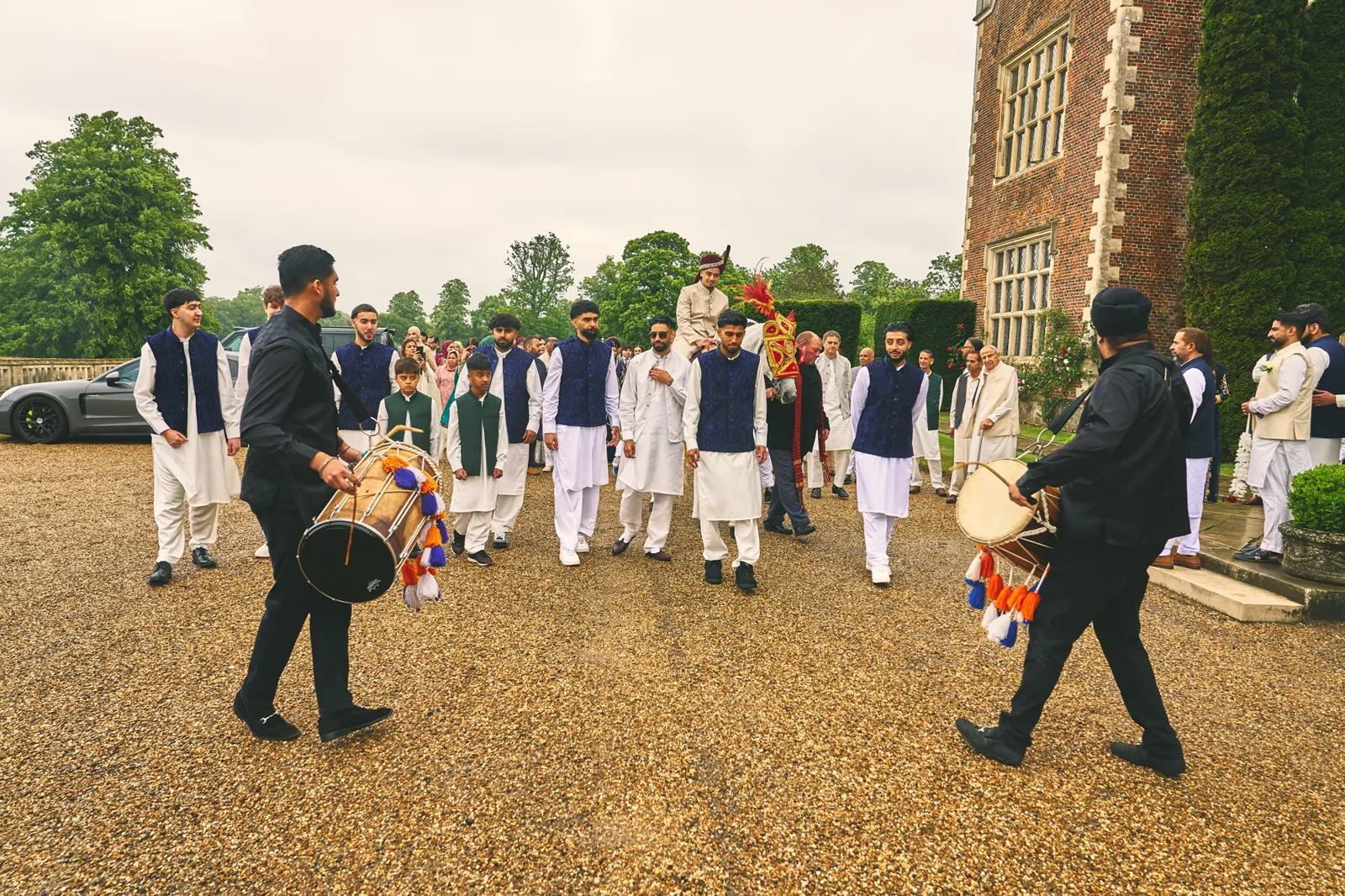 Two dhol players leading a baraat outside a country house