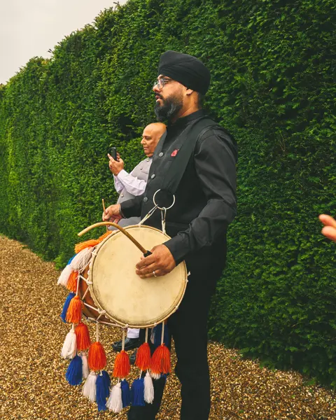 Dhol player in black leading a baraat